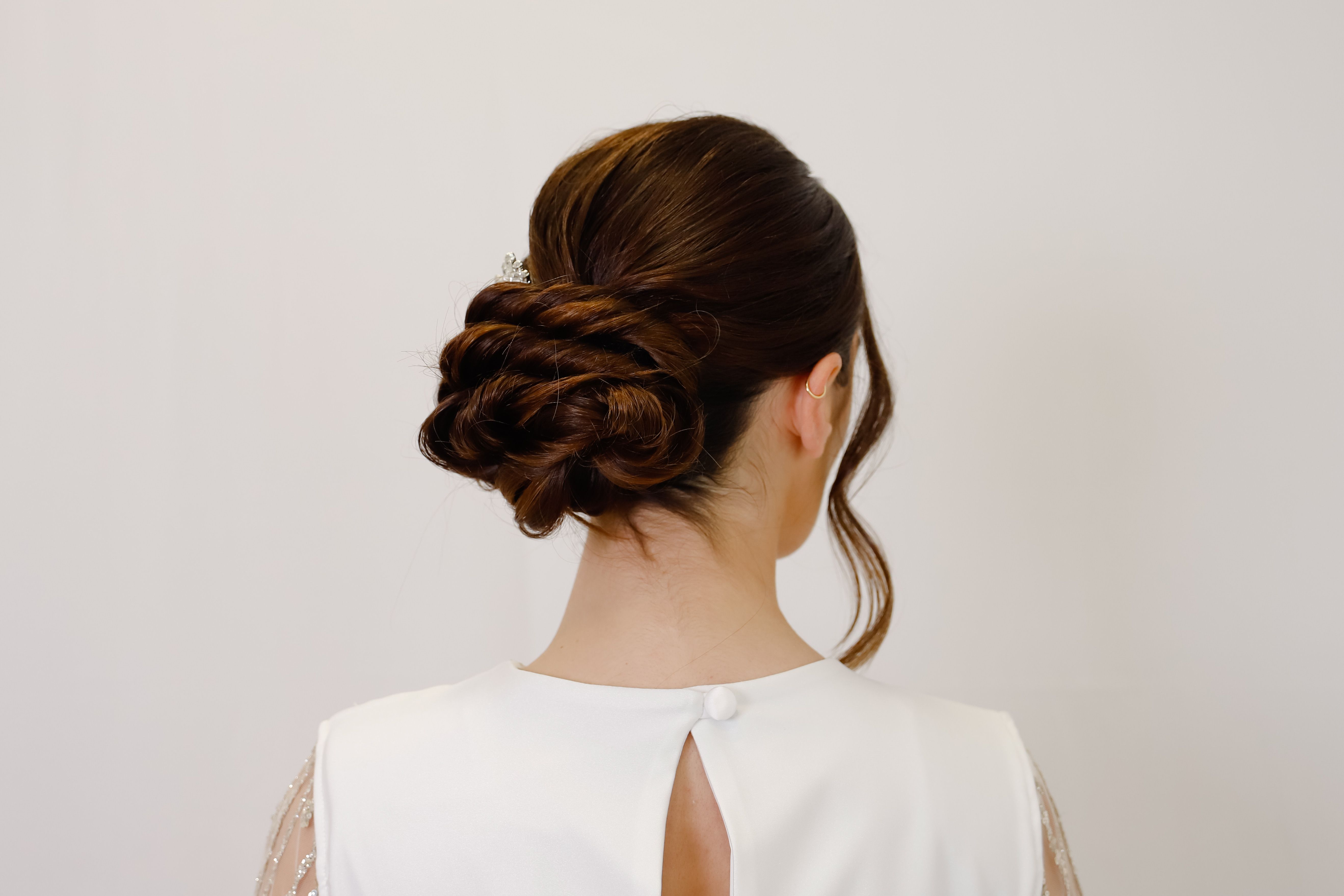 Close rear view of a dark-blonde braided chignon receiving a final adjustment