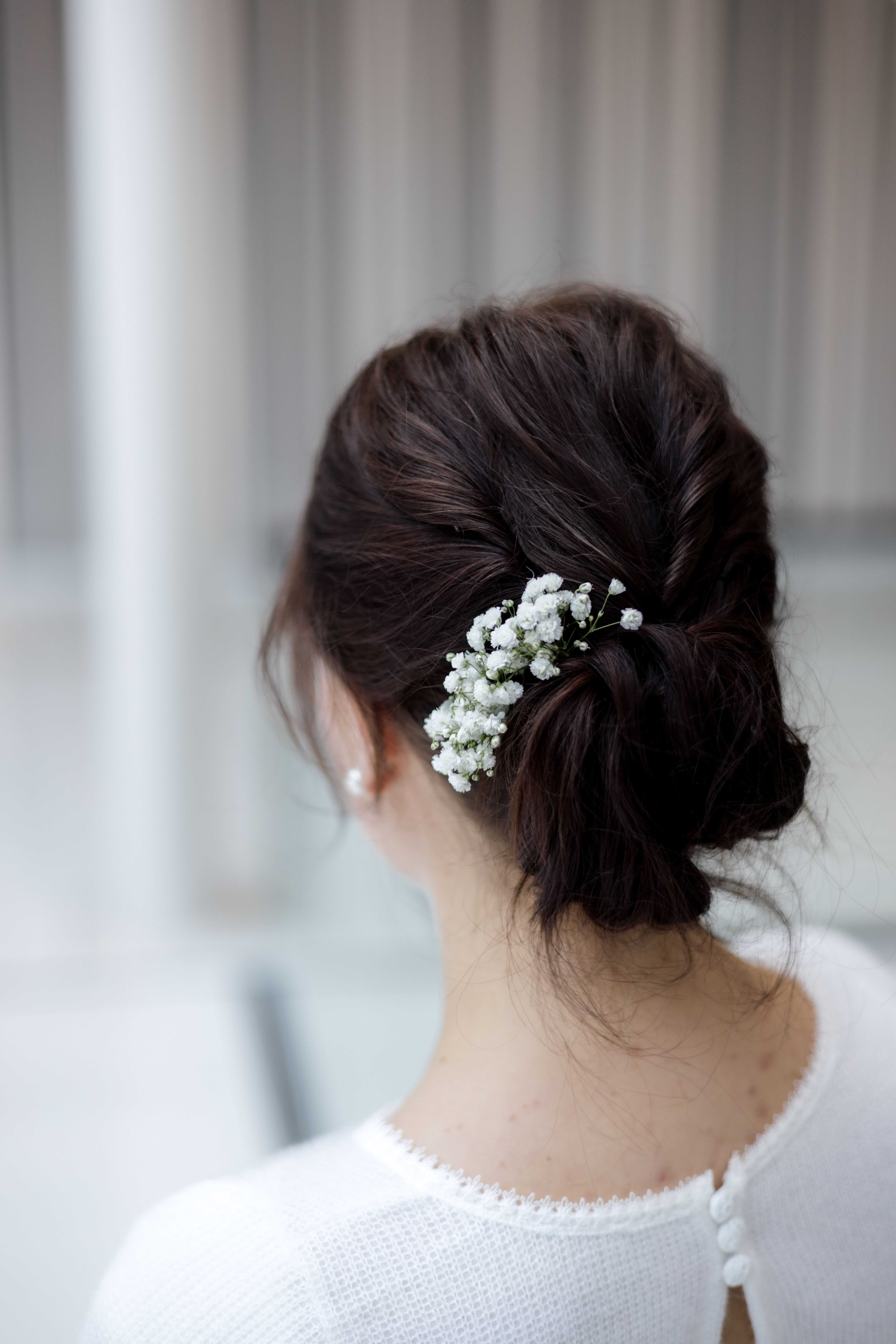 Rear three-quarter view of an intricate brunette low bun with pearl pins