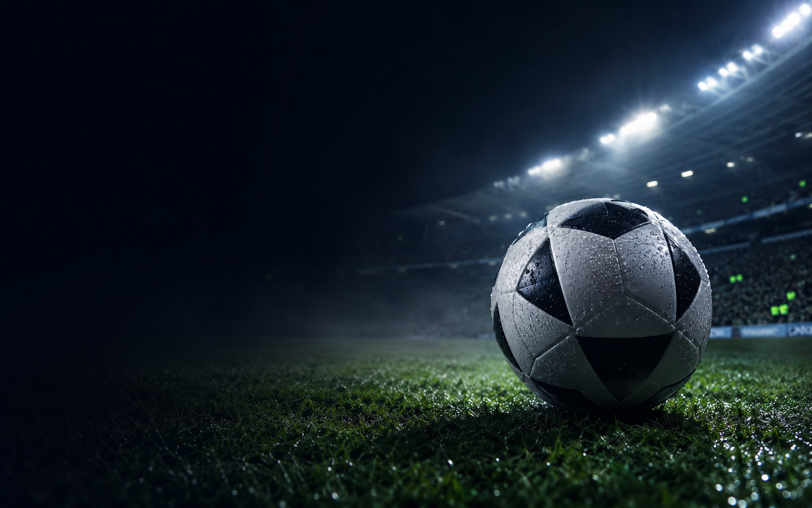 A football on a rain-soaked pitch beneath stadium lights
